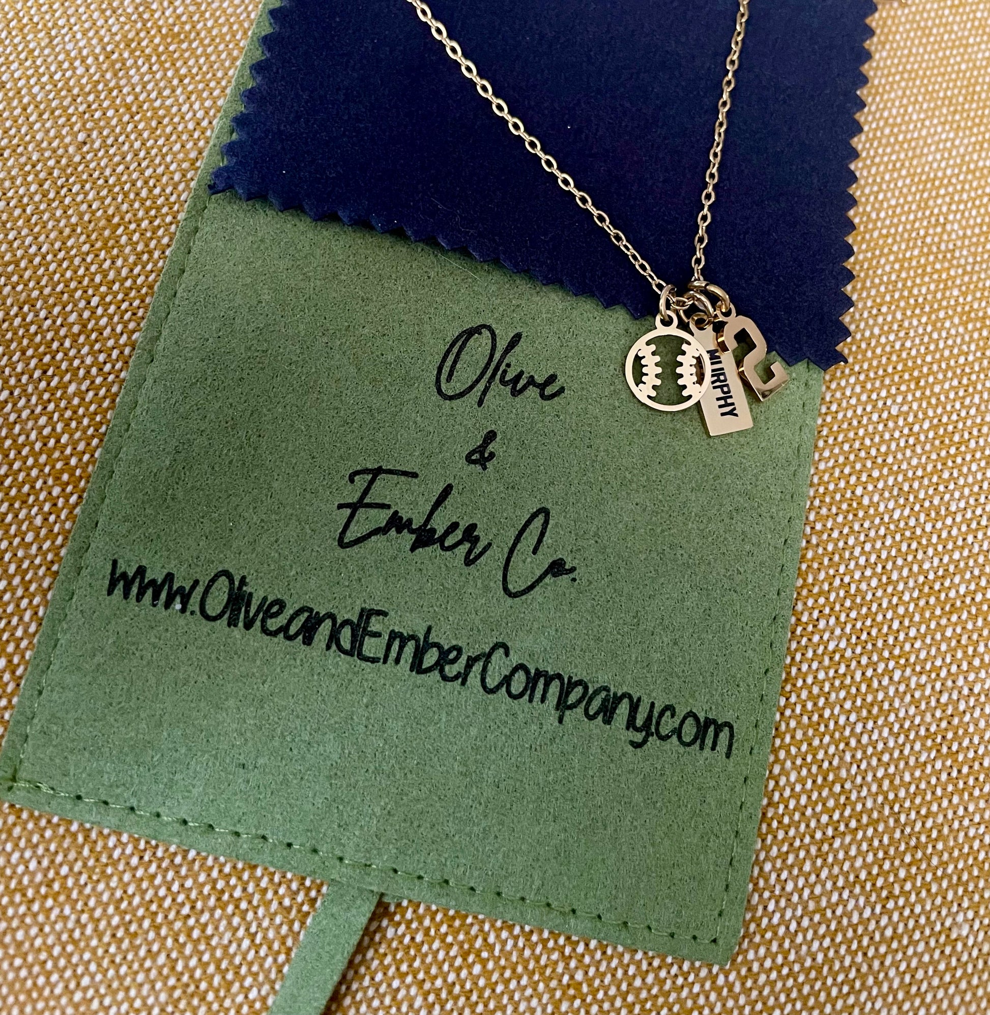 Necklace with charms on a green engraved microfiber jewelry pouch with 'Olive & Ember Co.' branding.