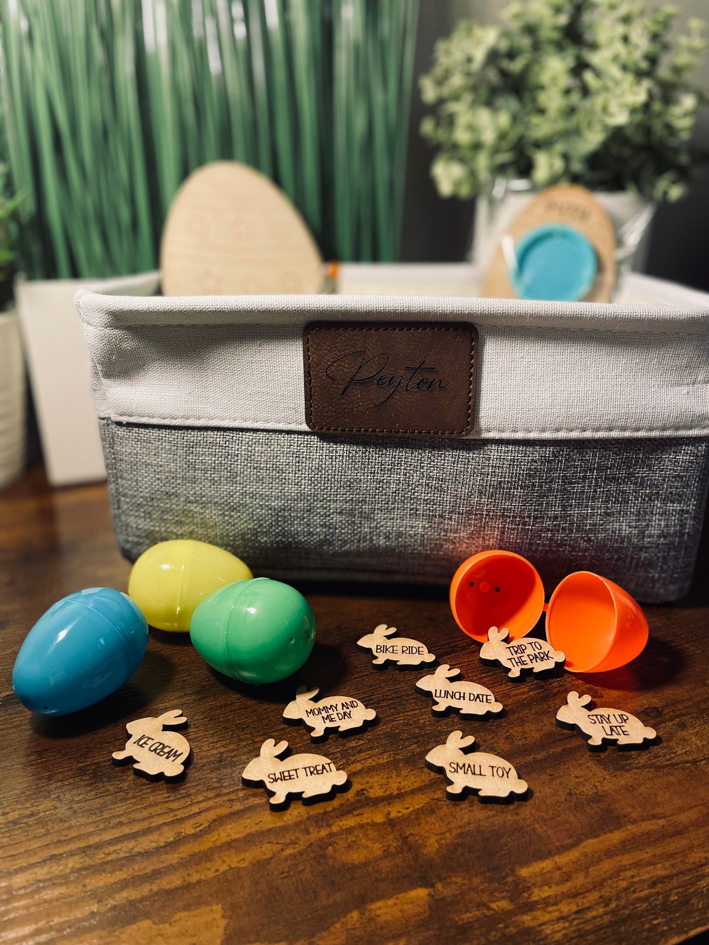 Colorful plastic eggs with wooden tags on a wooden surface, next to a fabric basket.