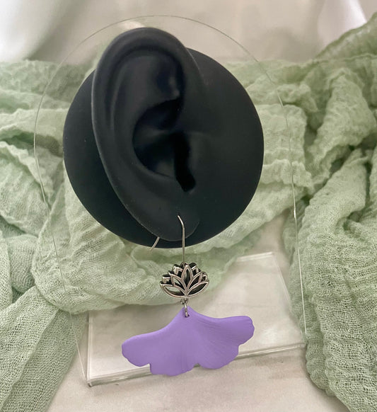 Purple gingko earring with a silver lotus design hanging from a black ear model on a green fabric background.