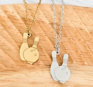 Two necklaces with a bowling ball and two pins as pendants both silver and gold plated on a wooden surface