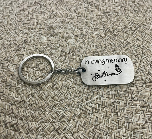 Silver keychain with 'In loving memory' engraved sitting on textured fabric background
