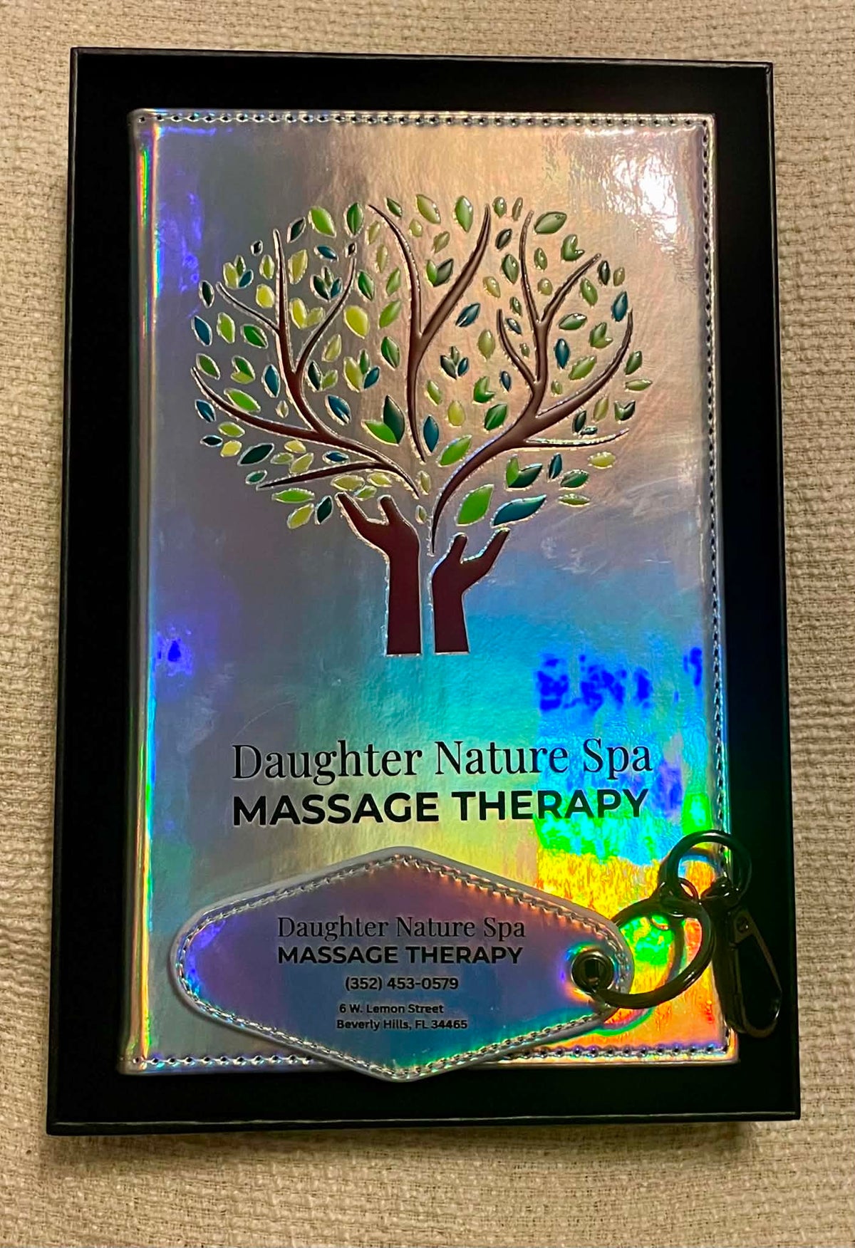UV printed journal showing Daughter Nature Spa Massage Therapy, featuring a metallic tree design and a matching keychain, displayed on a beige textured fabric background.